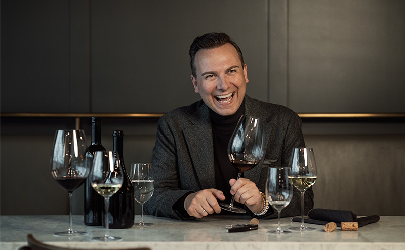 Star chef Tim Raue at an elegantly set table with handmade Enoteca wine glasses by Zwiesel Glas, filled with red and white wine; modern, stylish bar setting.