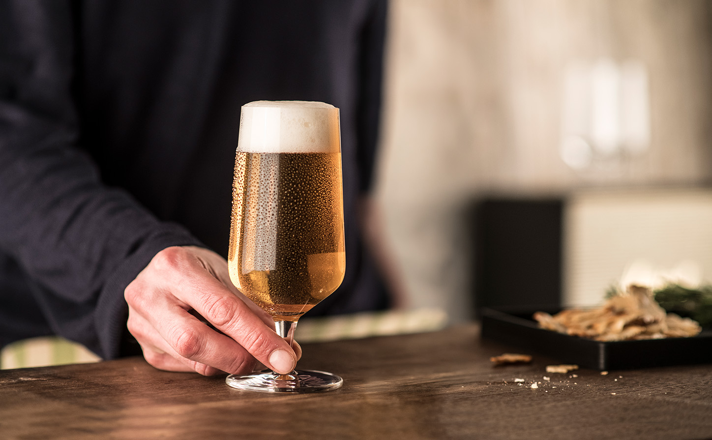 Schott Zwiesel Beer Basic pilsner glass filled with pale pilsner beer and a fine foamy head on a bar counter.
