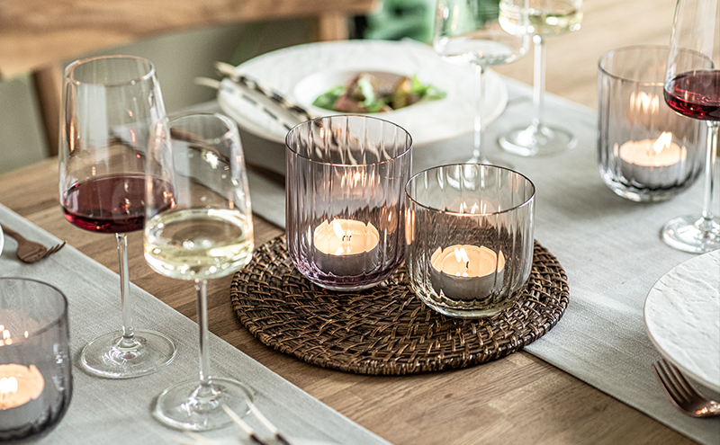 Set table with Dialogue vases by Zwiesel Glas used as lanterns with tealights, plus filled red and white wine glasses from the Vivid Senses series; a relaxed, inviting setting.