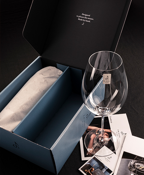 Handmade Enoteca glass by Zwiesel Glas on a table, with leaflets and an open two-piece box; the second glass wrapped in tissue paper.