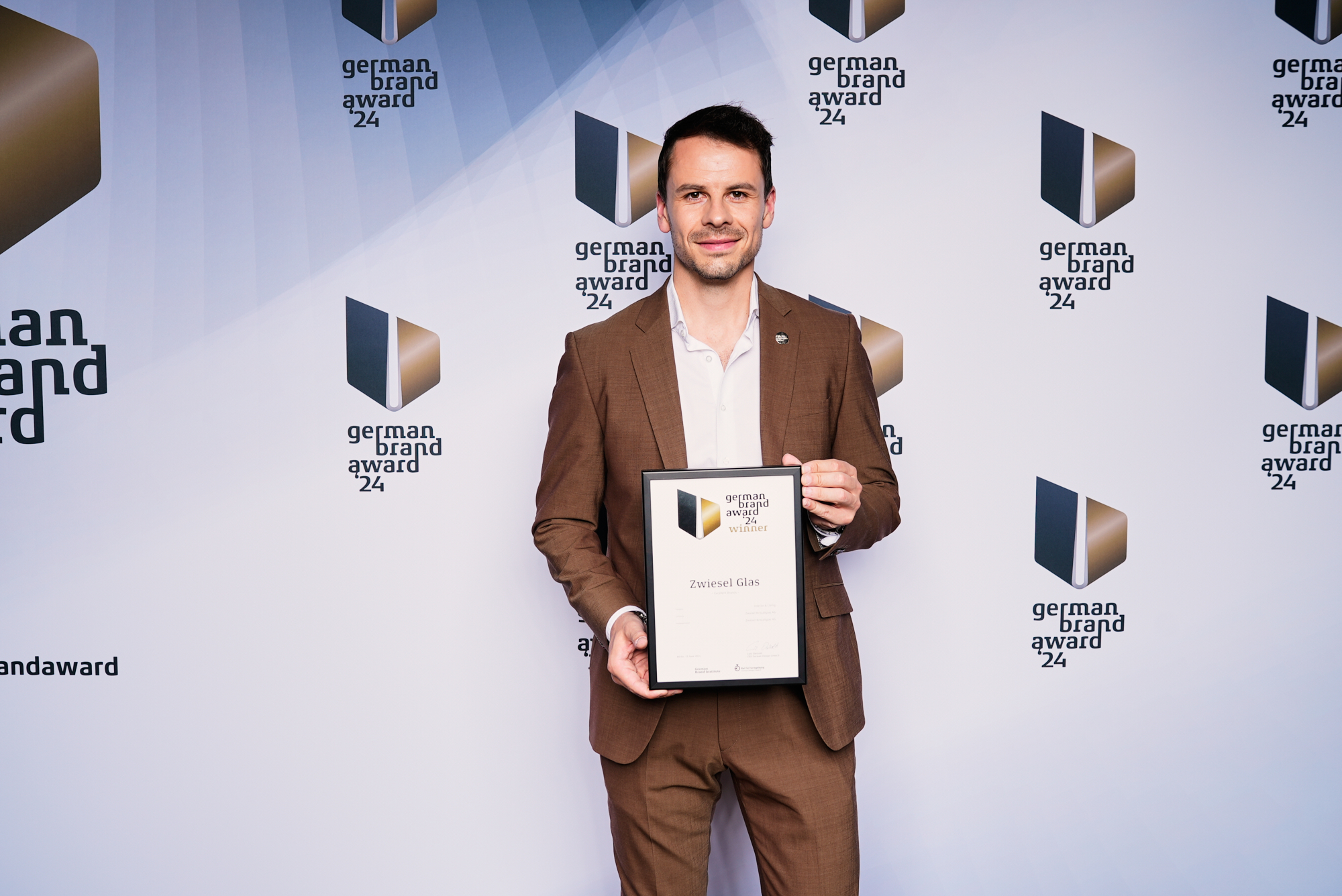 Foto von Michael Eichinger, der die Auszeichnung mit dem German Brand Award 2024 vor einer Wand mit Logos hält.