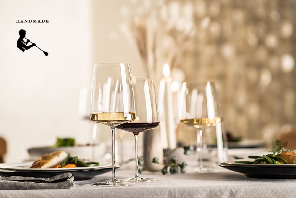 A festively laid table with handmade wine glasses from the Simplify series by Zwiesel Glas, filled with white and red wine, surrounded by food, candles, and stylish decoration.