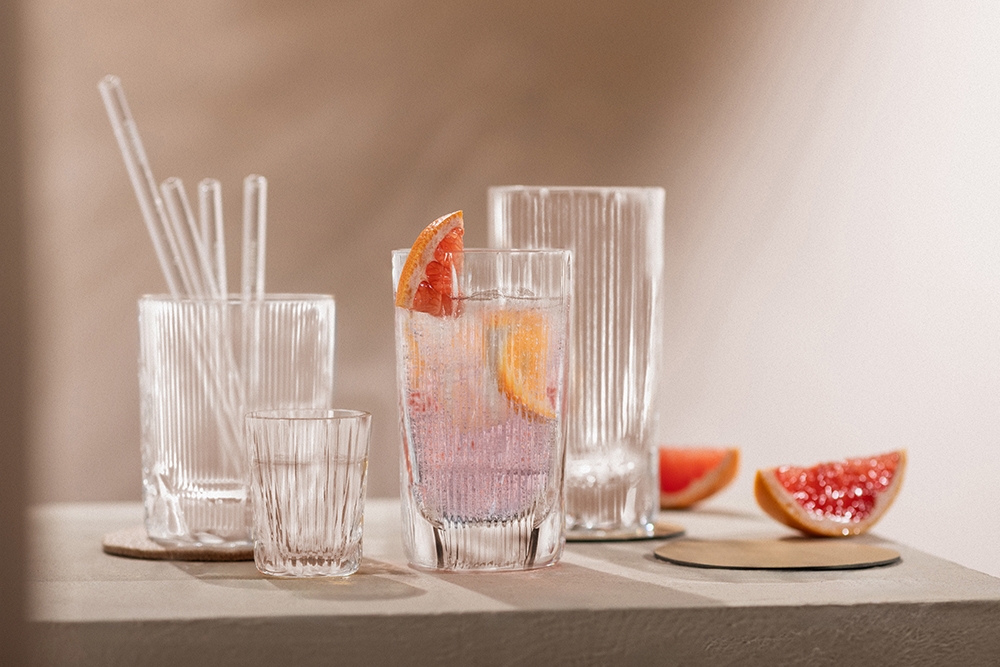 Verschillende cocktailglazen uit de serie Fave & Age met drankjes en rietjes staan op een tafel, ernaast liggen stukjes grapefruit.