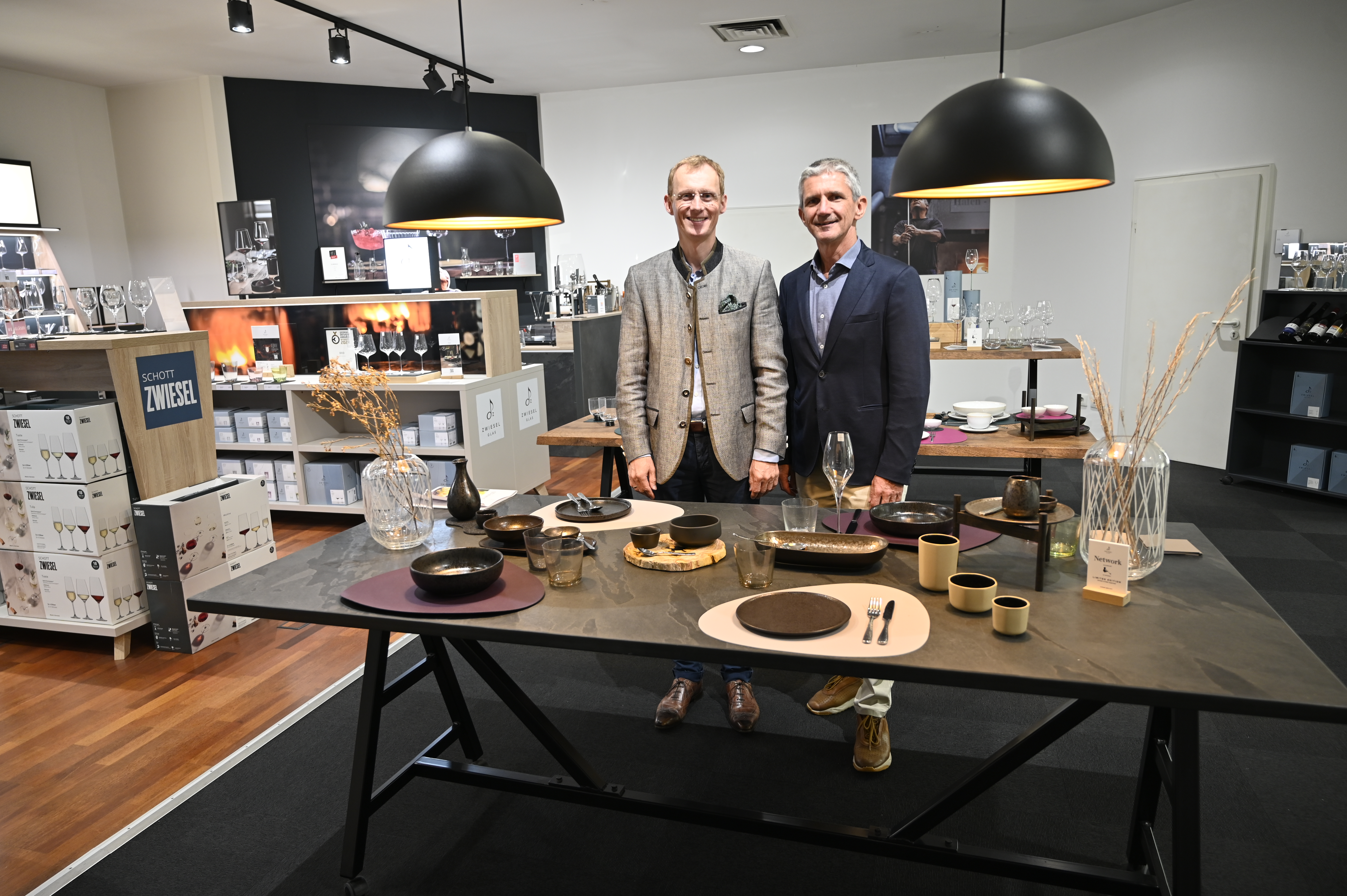 Prof. Andreas Buske und Helmar Hipp stehen an einem dekorierten Tisch in einem Showroom mit Gläsern und Geschirr. 