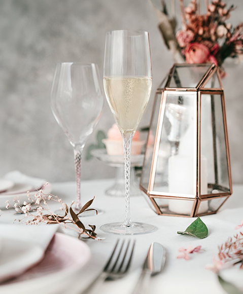 Elegant “Spirit” champagne glass on a decorated table with floral accents and a second glass behind.