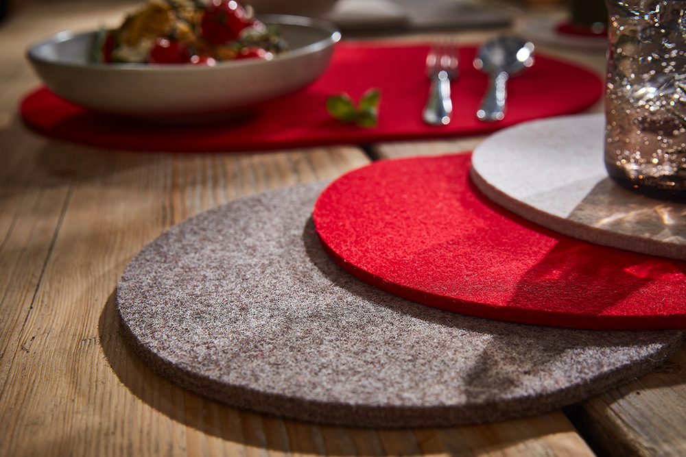 Sets de table ronds en feutre de laine gris, rouges et blancs sur une table en bois.