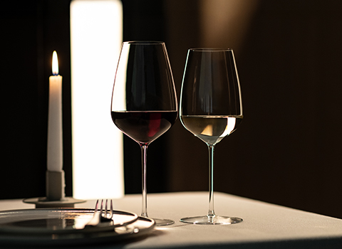 Two wine glasses for red and white wine, designed by Antoine Petrus, on a table, with a candle in the background.