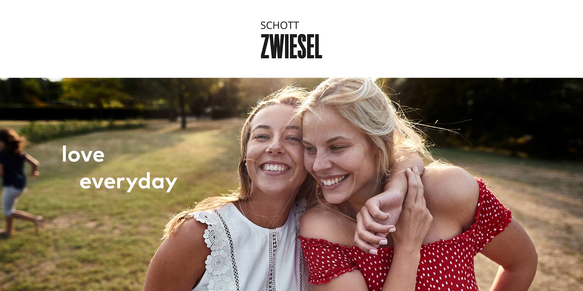 Zwei Personen in sommerlicher Kleidung umarmen sich auf einer Wiese bei Sonnenlicht, Text Schott Zwiesel „love everyday“.