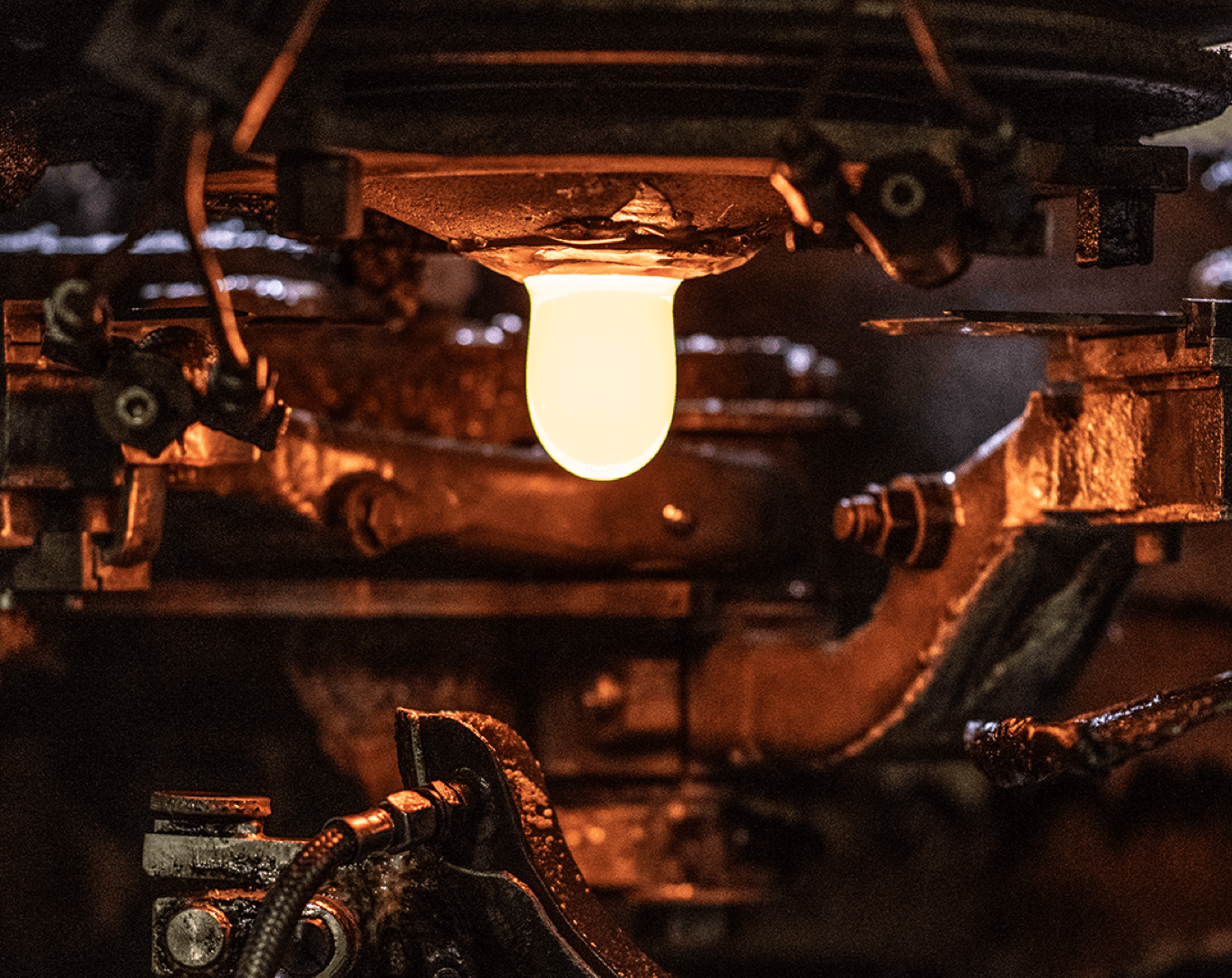 Eine leuchtende, heiße Glasmasse wird maschinell in einer industriellen Glasfertigungsanlage geformt.