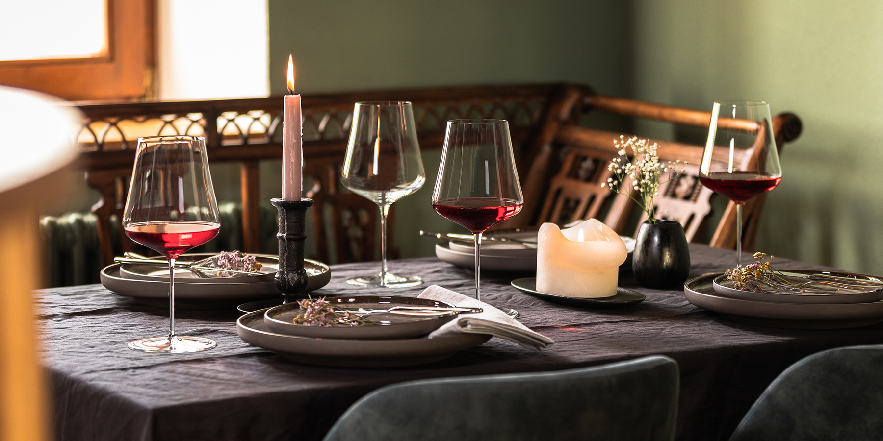 Table festive dressée avec plusieurs verres Duo de Zwiesel Glas, certains remplis de vin rouge, bougies et assiettes sur une nappe sombre.