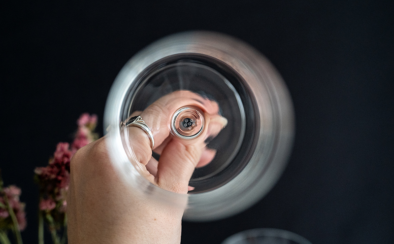 Une main avec une bague est visible à travers un verre depuis le haut.