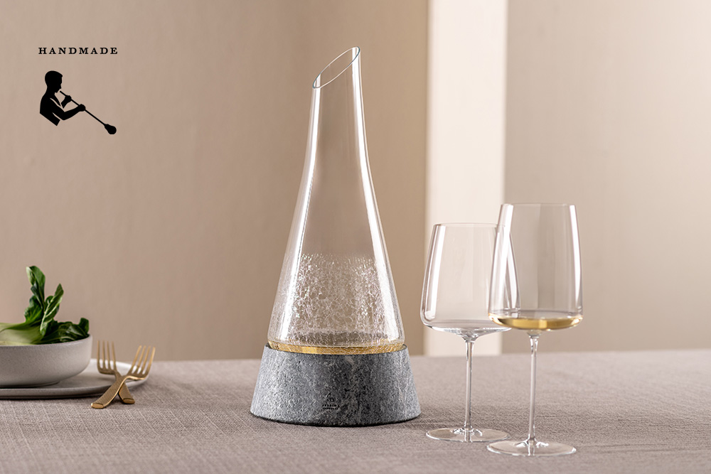 A Symbiosis decanter on a stone base and two Simplify wine glasses on a table