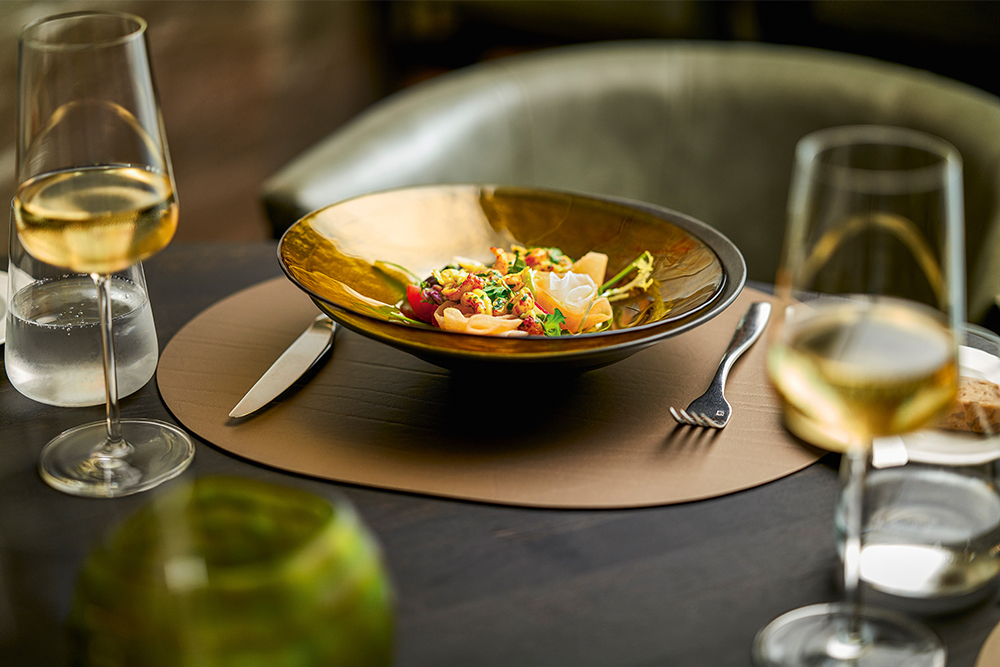 Set de table Letherixx marron clair, sur lequel sont posés une assiette avec de la nourriture et des verres à vin Vervino.