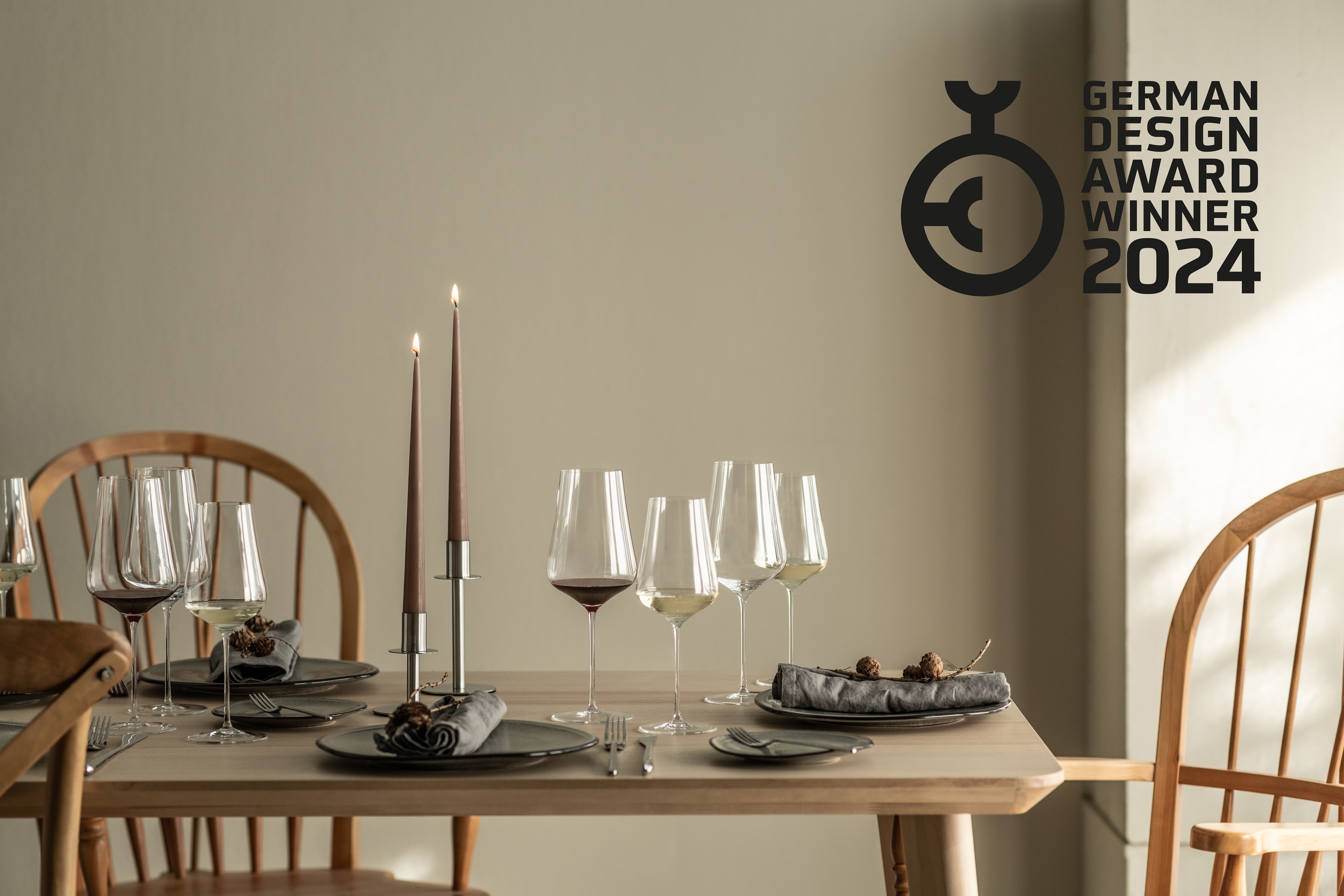 Festlich gedeckter Holztisch mit Kerzen, Gläsern und Tellern. Logo des German Design Award 2024 rechts oben. 