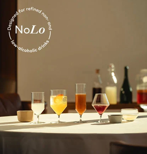 Glasses filled with coloured, non-alcoholic drinks on a table in a restaurant. The NoLo symbol is visible in the top left corner of the image. It indicates that the drinks have a low or no alcohol content.