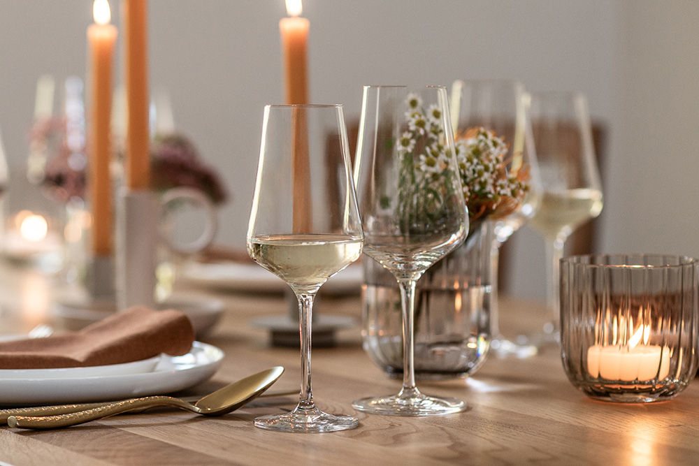 Wine glasses from the Bouquet range on a laid table. Candles and a lantern from the Dialogue range in the background.