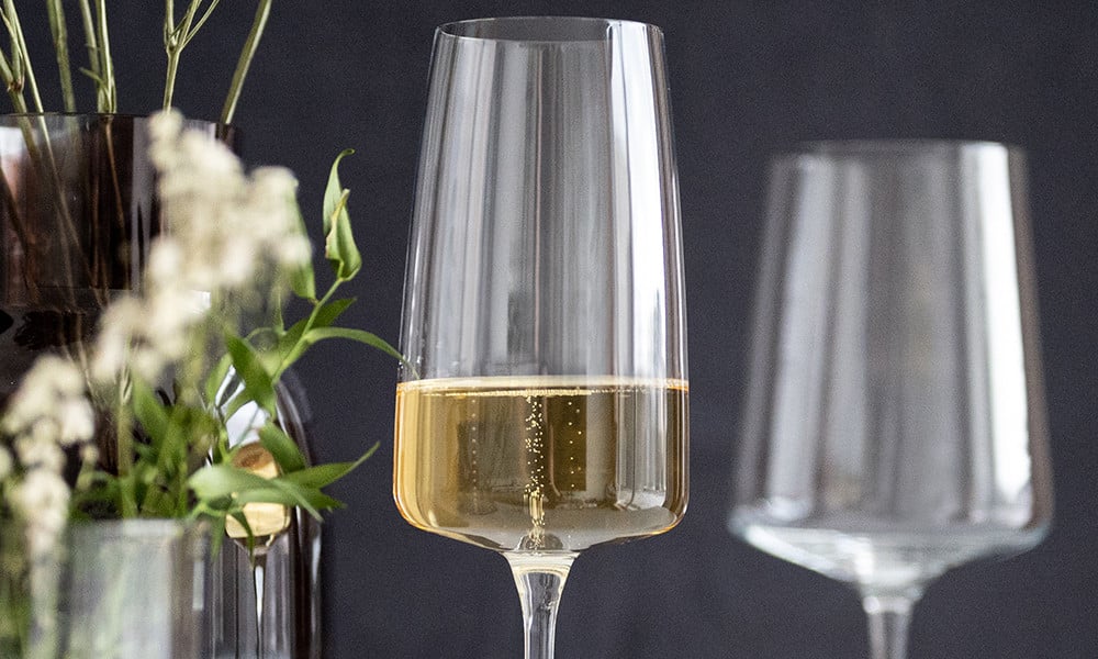 Un verre de vin blanc est posé à côté d'un verre vide et de fleurs.