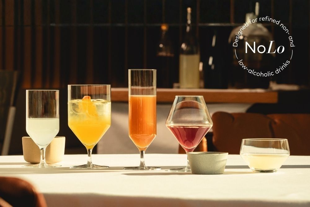 Glasses filled with colorful non-alcoholic drinks on a table in a restaurant. The NoLo symbol appears in the upper right corner of the image, indicating that the drinks contain little or no alcohol.