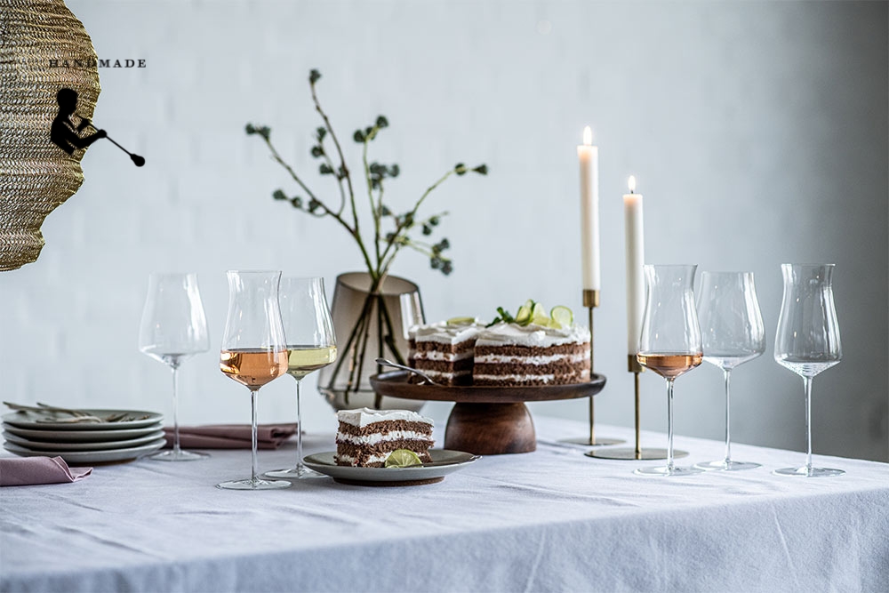 Handmade wine glasses from the The Moment series by Zwiesel Glas on a brightly set coffee table with cake, plates, candles, and aesthetic decoration in the background.