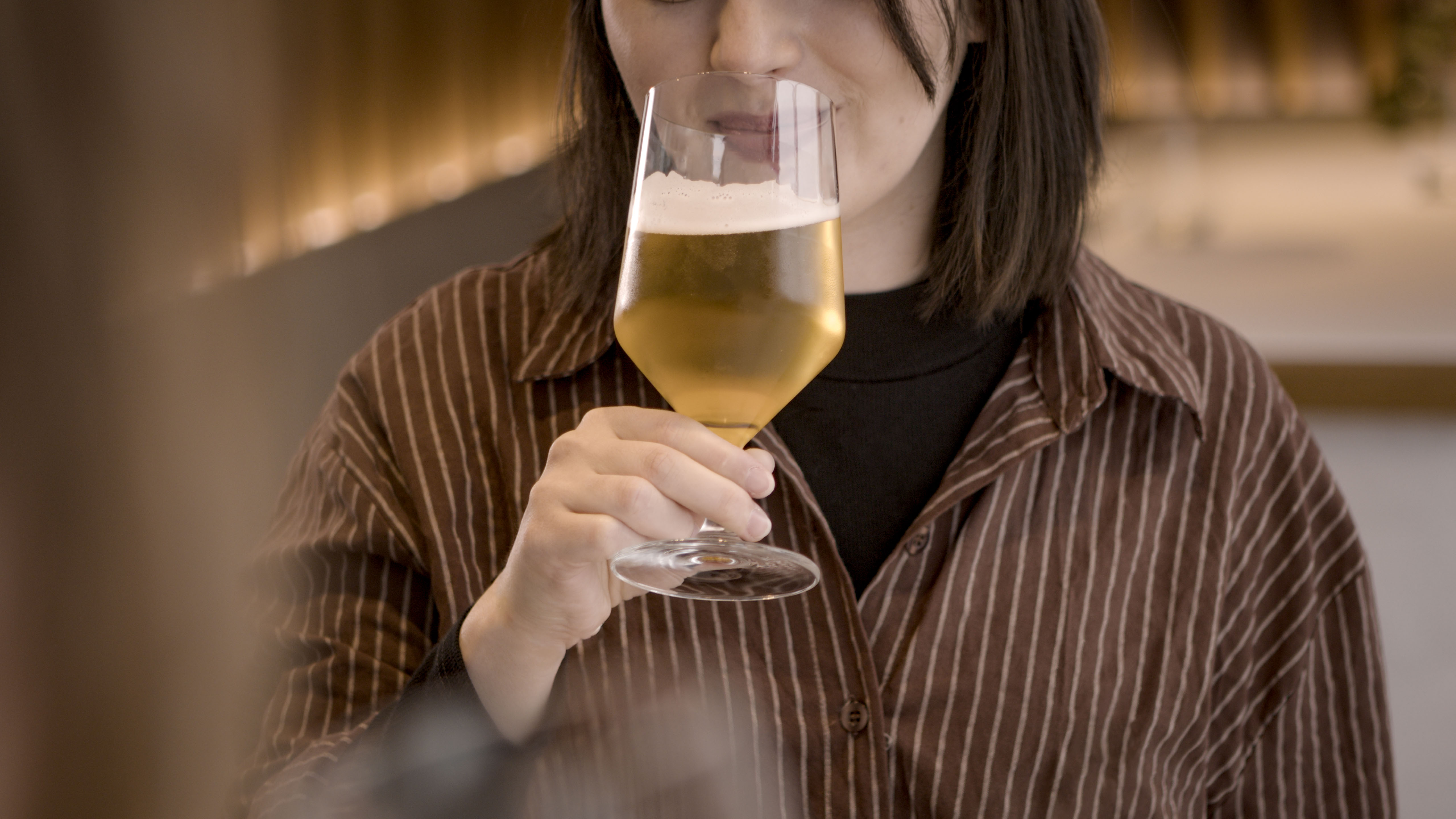 Person hält ein Glas mit hellem Bier in einer Restaurantumgebung.