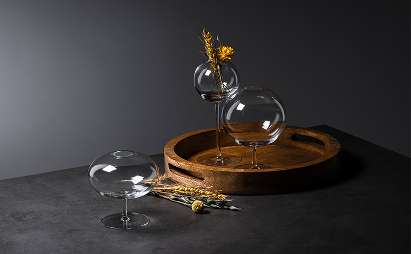 Three handmade Fleur vases by Zwiesel Glas in different sizes, arranged on a dark table with a wooden tray, dried flowers, and a stylish, modern background.