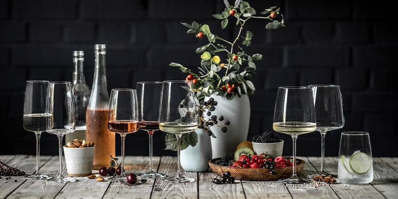 Une table avec des verres, des bouteilles, un vase avec des fleurs et des fruits.