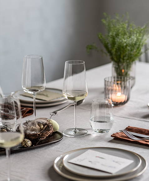 Vervino white wine glasses by Zwiesel Glas, filled with white wine, on a simply set Easter table with natural décor, nest and candle.