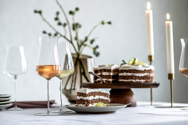 Verre à champagne moderne tout-en-un The Moment de Zwiesel Glas à côté d’une part de gâteau et d’autres verres sur une table à café dressée avec style.